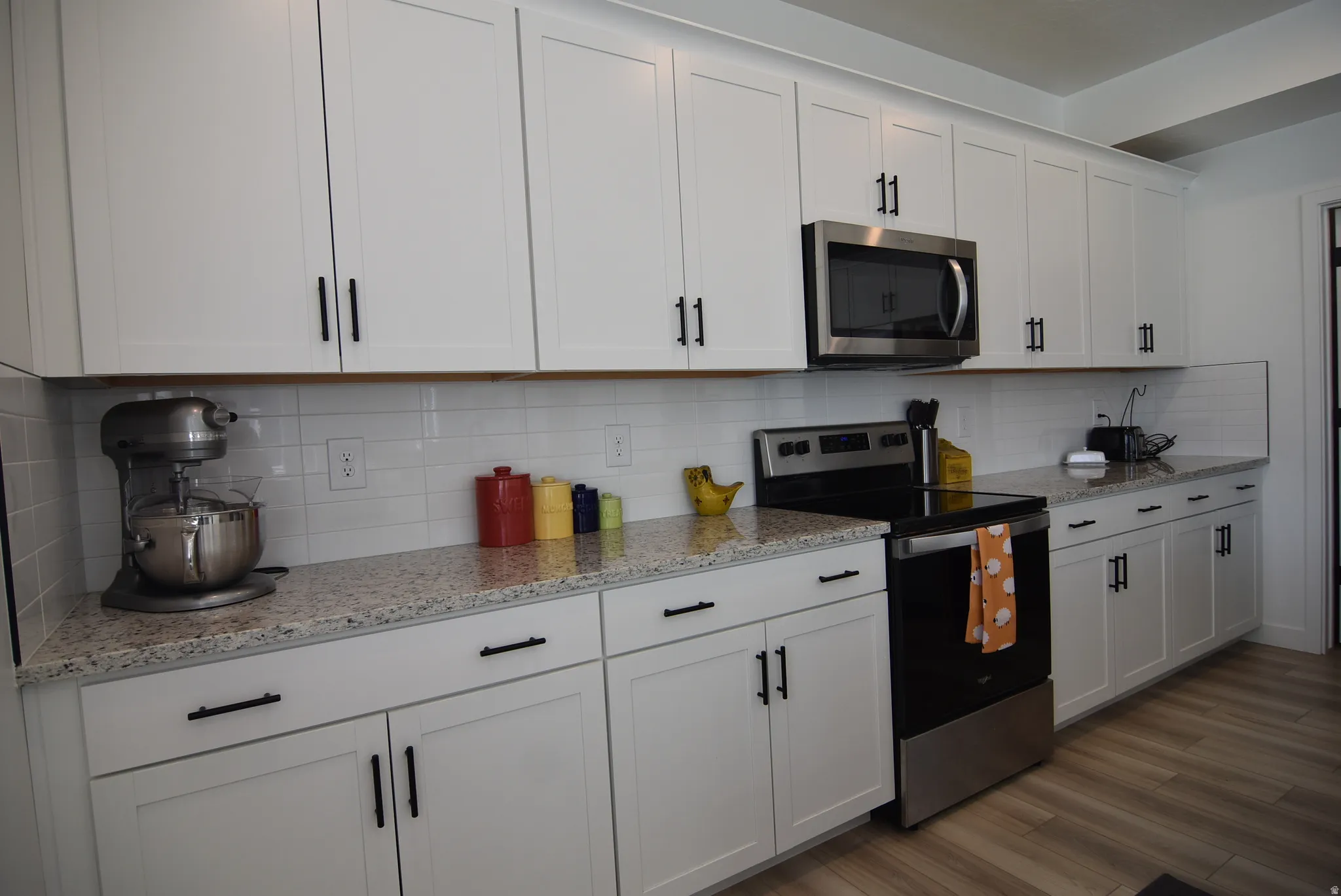 Modern kitchen featuring white shaker cabinetry with black hardware, light-toned speckled countertops, white subway tile backsplash, and stainless steel appliances