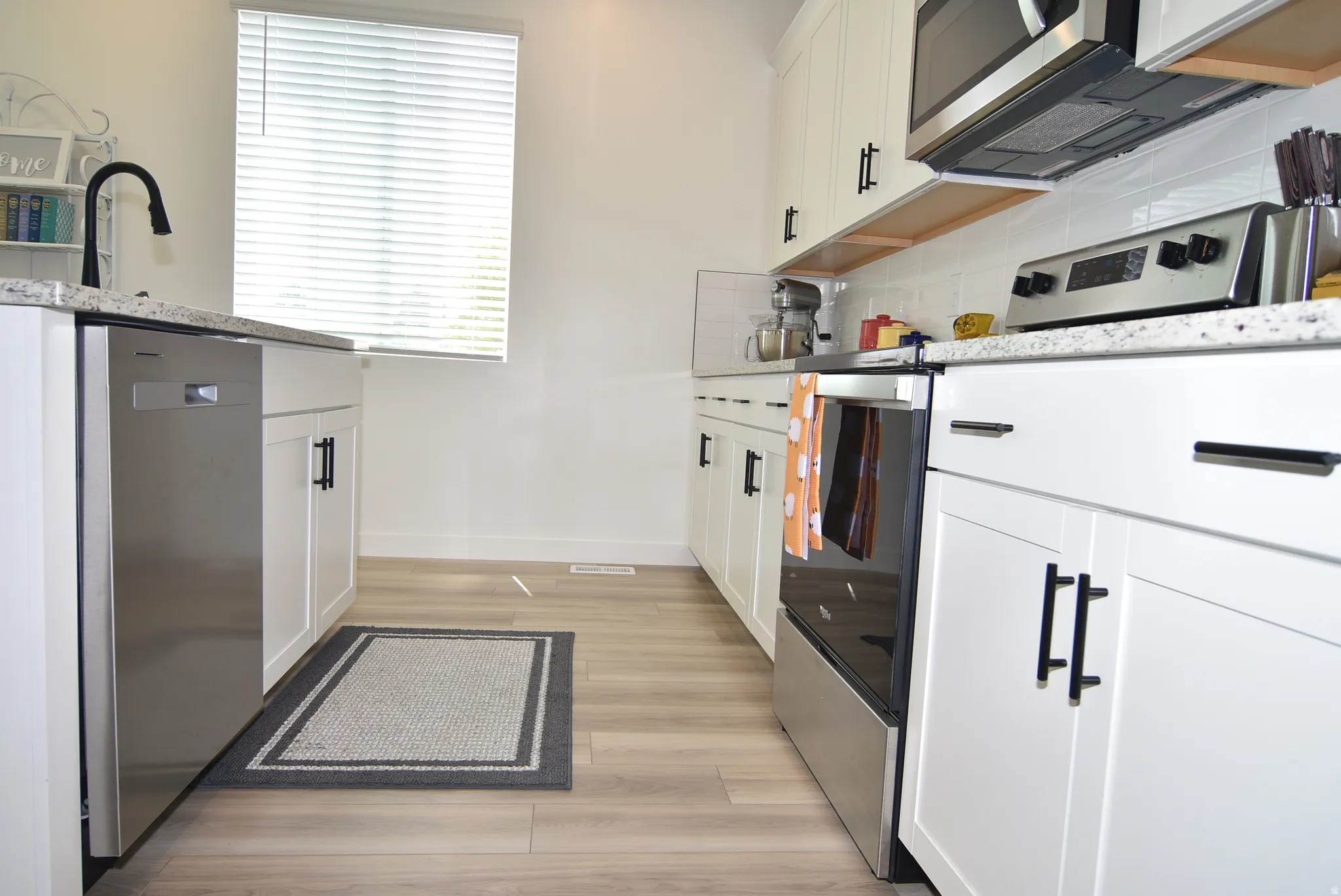 Modern kitchen featuring light wood-finish flooring, white cabinetry with matte black hardware, stone-finish countertops, stainless steel appliances, and a subway tile backsplash