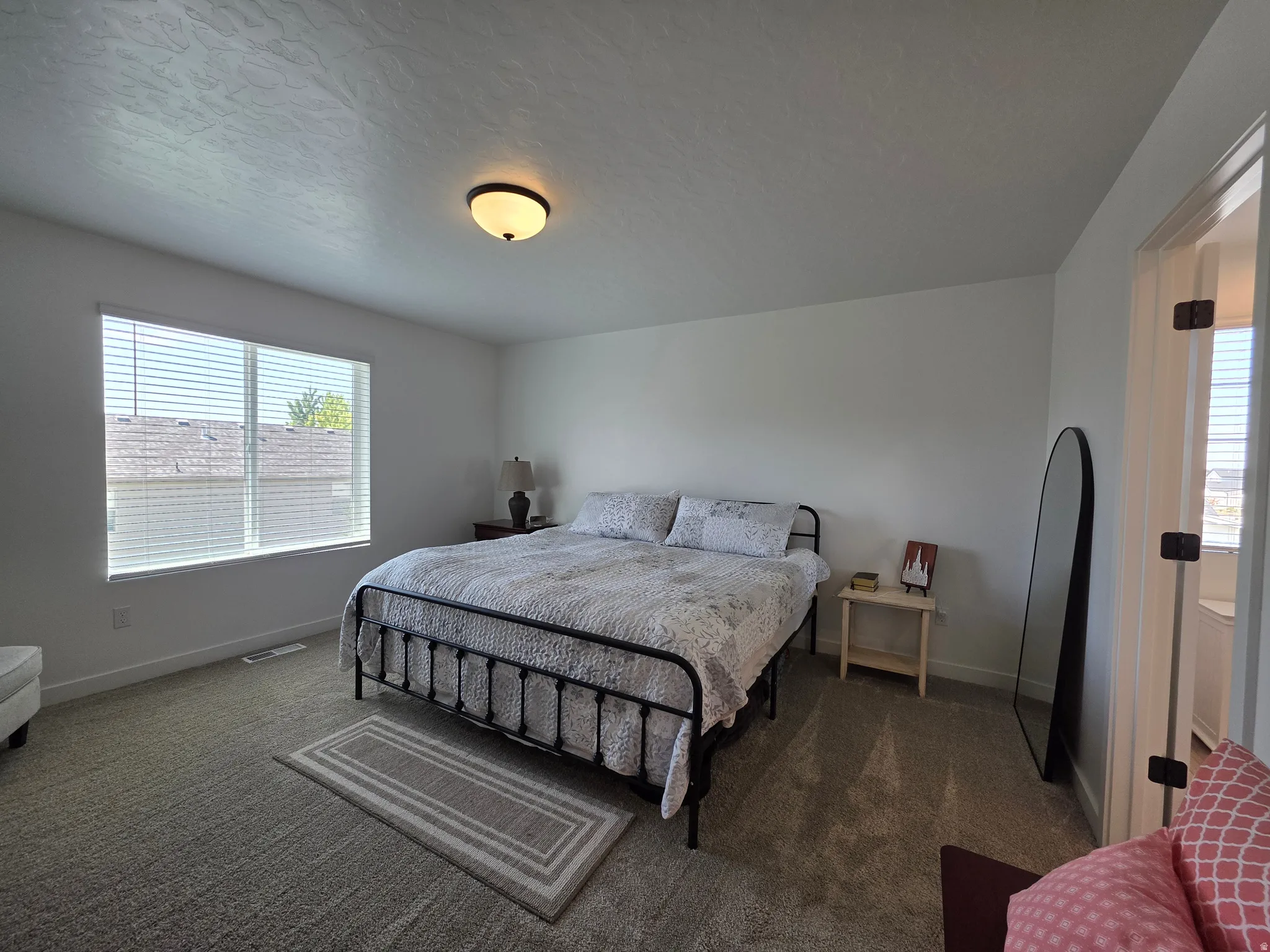 Carpeted bedroom featuring a large window with blinds, white walls, and a ceiling-mounted light fixture