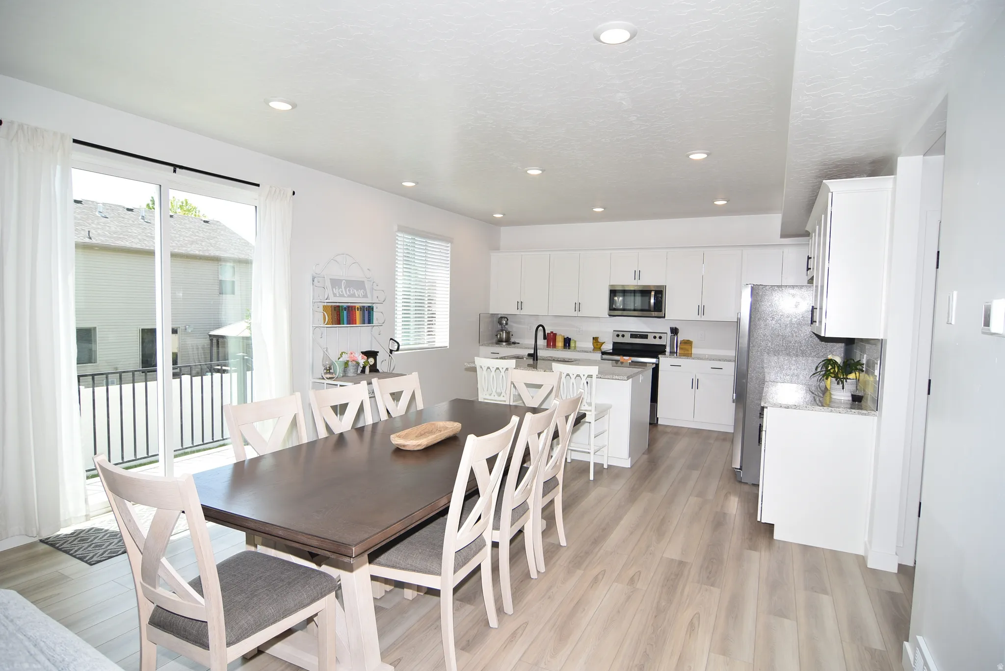 Open-concept kitchen and dining area featuring light wood-finish flooring, white cabinetry, stainless steel appliances, and recessed lighting