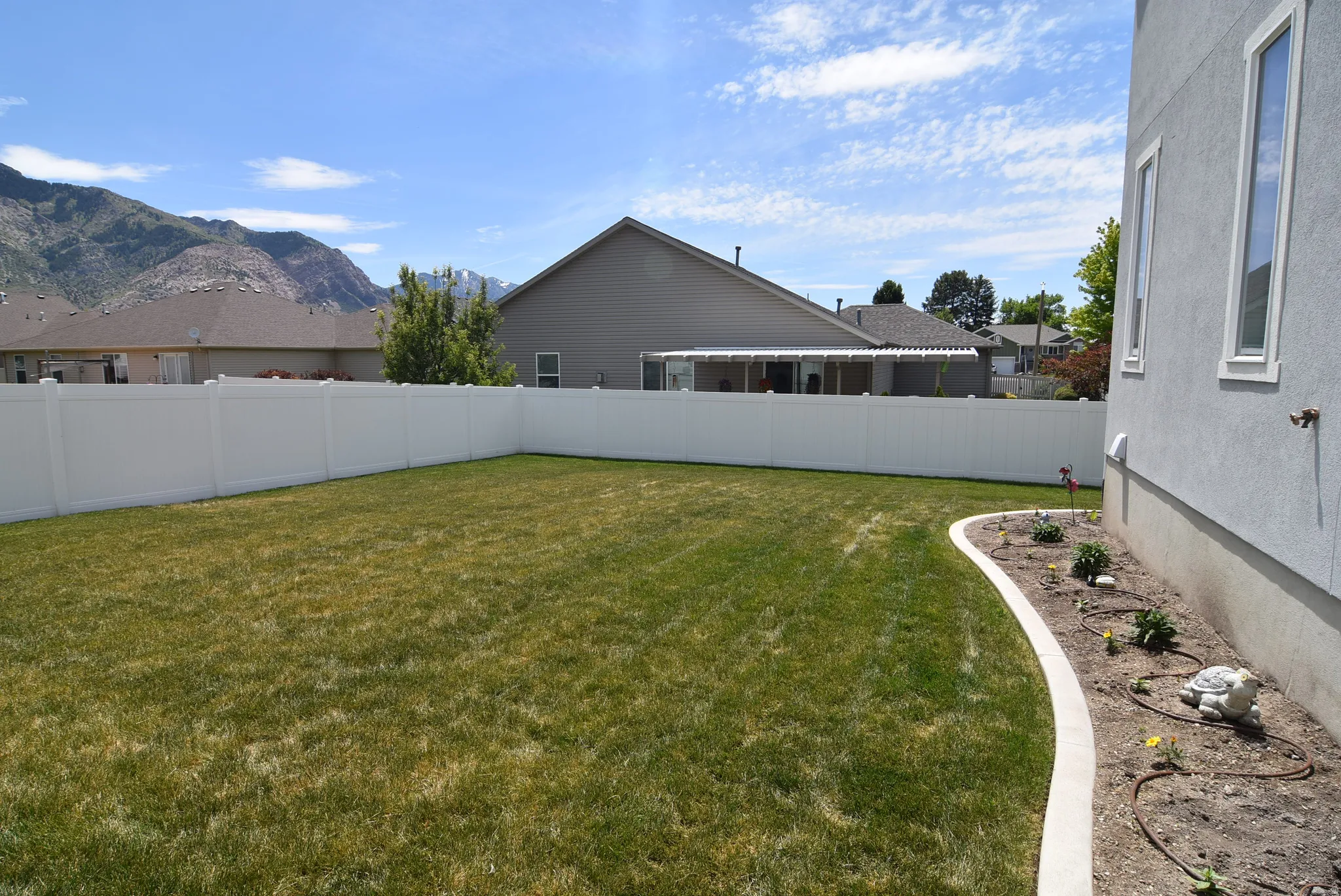 Expansive rear yard featuring a manicured lawn, full vinyl privacy fencing, and a curved planting bed