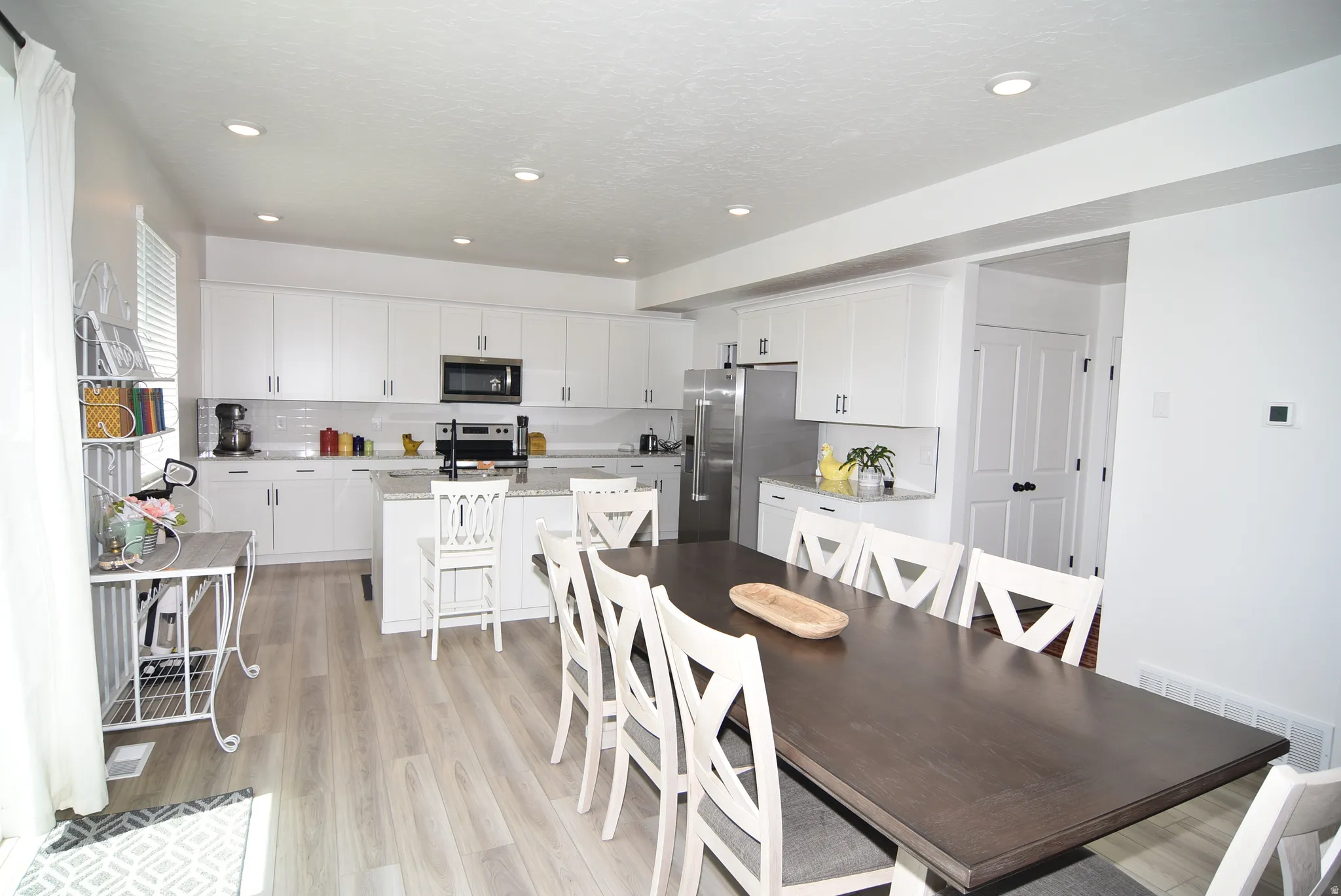 Open-concept kitchen and dining area featuring white cabinetry, stainless steel appliances, light-toned wood-finish flooring, recessed lighting, and a kitchen island with seating