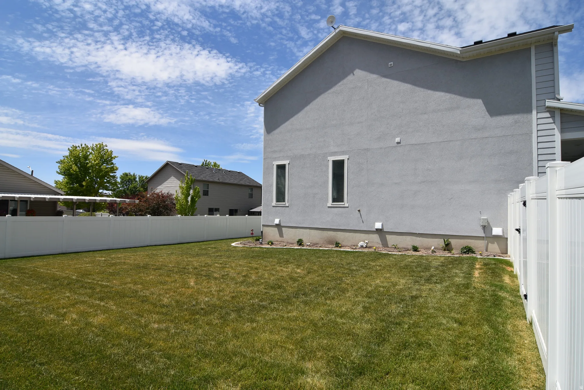Expansive backyard featuring a manicured lawn, full privacy fencing, and a modern stucco exterior
