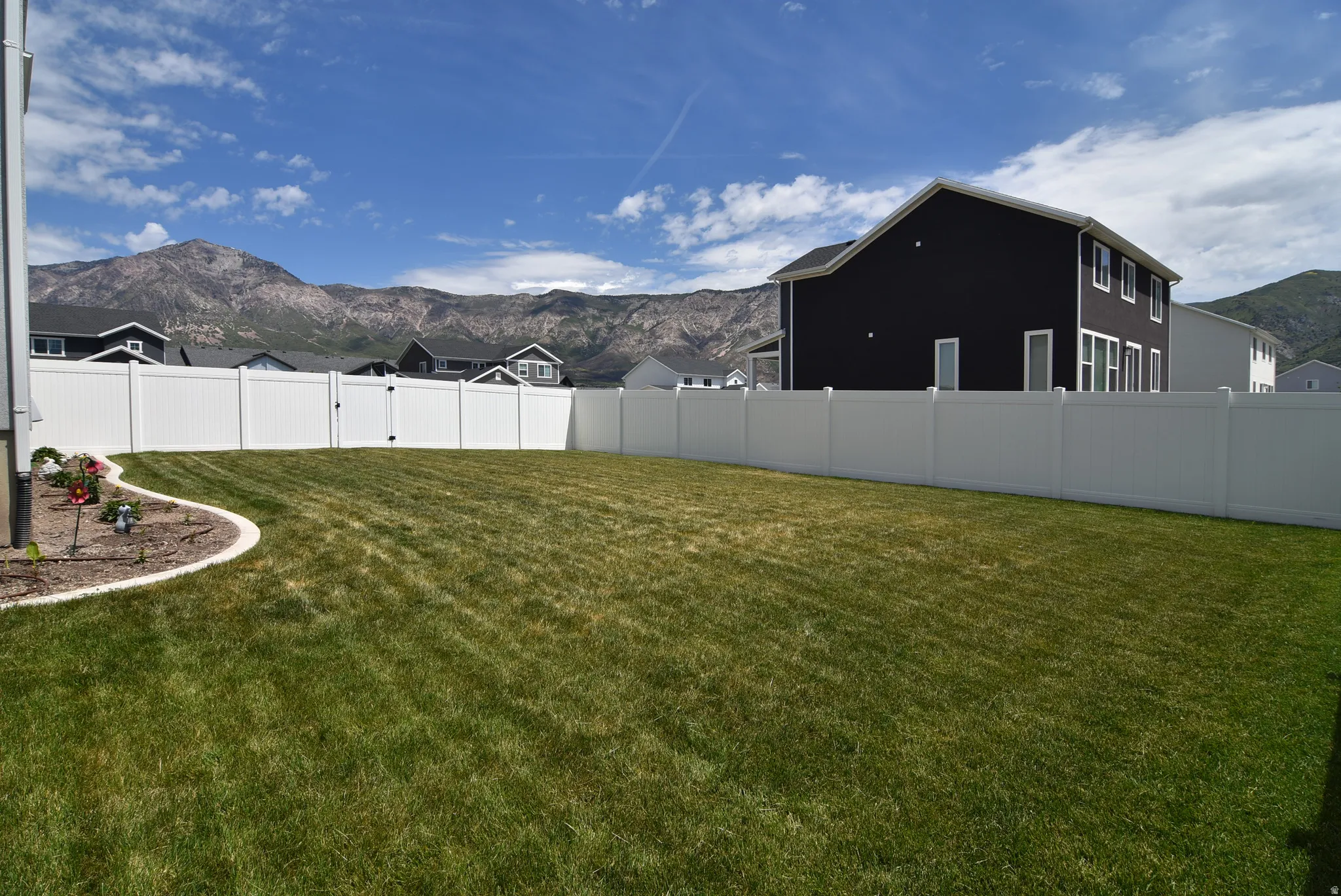 Spacious backyard with a vibrant green lawn, white vinyl fencing, and a curved garden bed