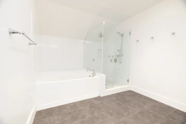 White-tiled bath and glass-enclosed shower with multiple shower heads