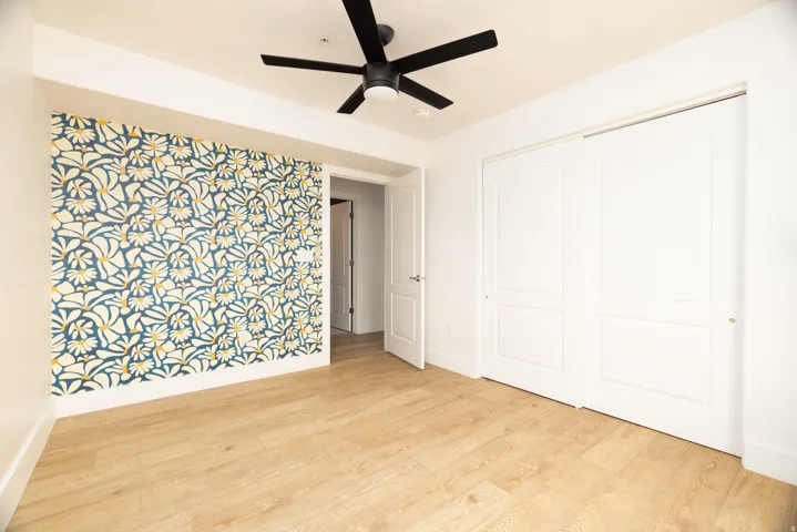 Accent wall featuring a botanical pattern, wood-finish flooring, white sliding closet doors, and a black ceiling fan