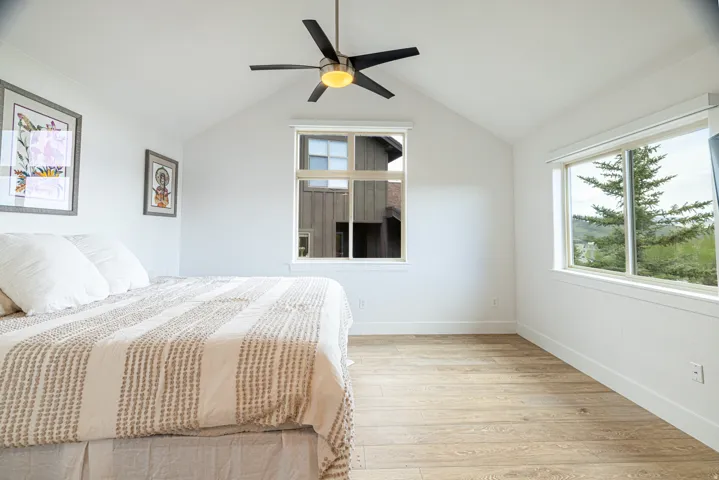Bright interior space featuring vaulted ceilings, wood-finish flooring, a contemporary ceiling fan with integrated lighting, and multiple windows providing ambient illumination