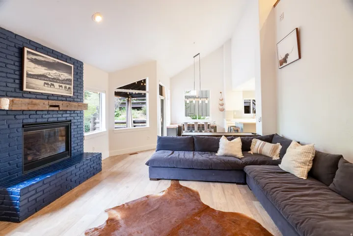 Spacious living area featuring a blue brick fireplace with a wood mantel, light wood-finish flooring, and high vaulted ceilings