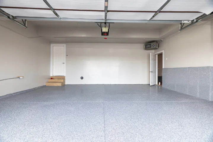 Spacious garage featuring a speckled epoxy flooring, painted walls, two access doors, and an overhead garage door mechanism