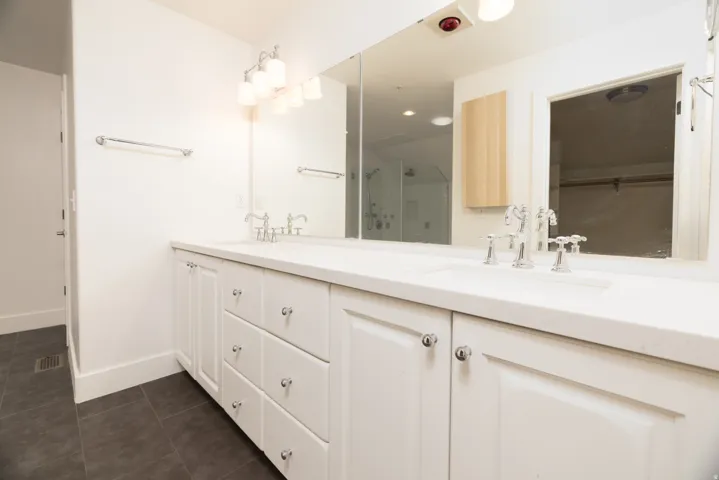 Double vanity with white cabinetry, integrated sinks, chrome fixtures, and a large wall-mounted mirror