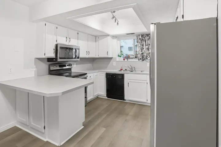 Kitchen featuring wood-finish flooring, white cabinetry with silver hardware, gray countertops, and stainless steel appliances including a microwave, range, and refrigerator
