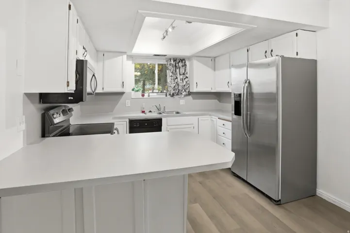 Kitchen featuring white cabinetry, light countertops, wood-finish flooring, stainless steel side-by-side refrigerator, and a built-in cooktop with oven