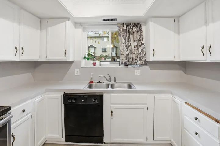 Kitchen featuring white cabinetry, light countertops, and a double basin stainless steel sink with a window overhead