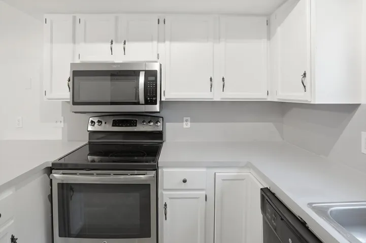 Kitchen featuring white cabinetry, light countertops, stainless steel microwave, electric range with a black ceramic cooktop, and a stainless steel sink