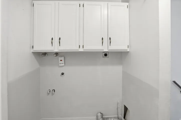 Dedicated laundry area featuring white upper cabinetry with dark hardware and essential plumbing hookups