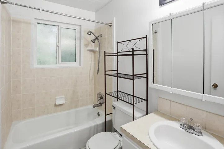 Bathroom featuring a white bathtub, ceramic tile surround with a window, white vanity with an integrated sink, and a mirrored medicine cabinet
