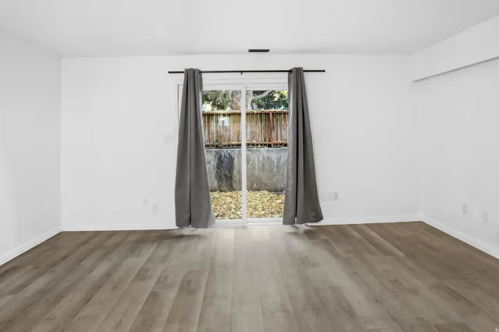 Spacious room featuring wood-finish flooring, white walls, and white baseboards