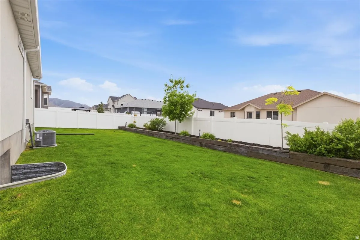 Expansive backyard featuring a manicured lawn, white vinyl fencing, and a tiered retaining wall