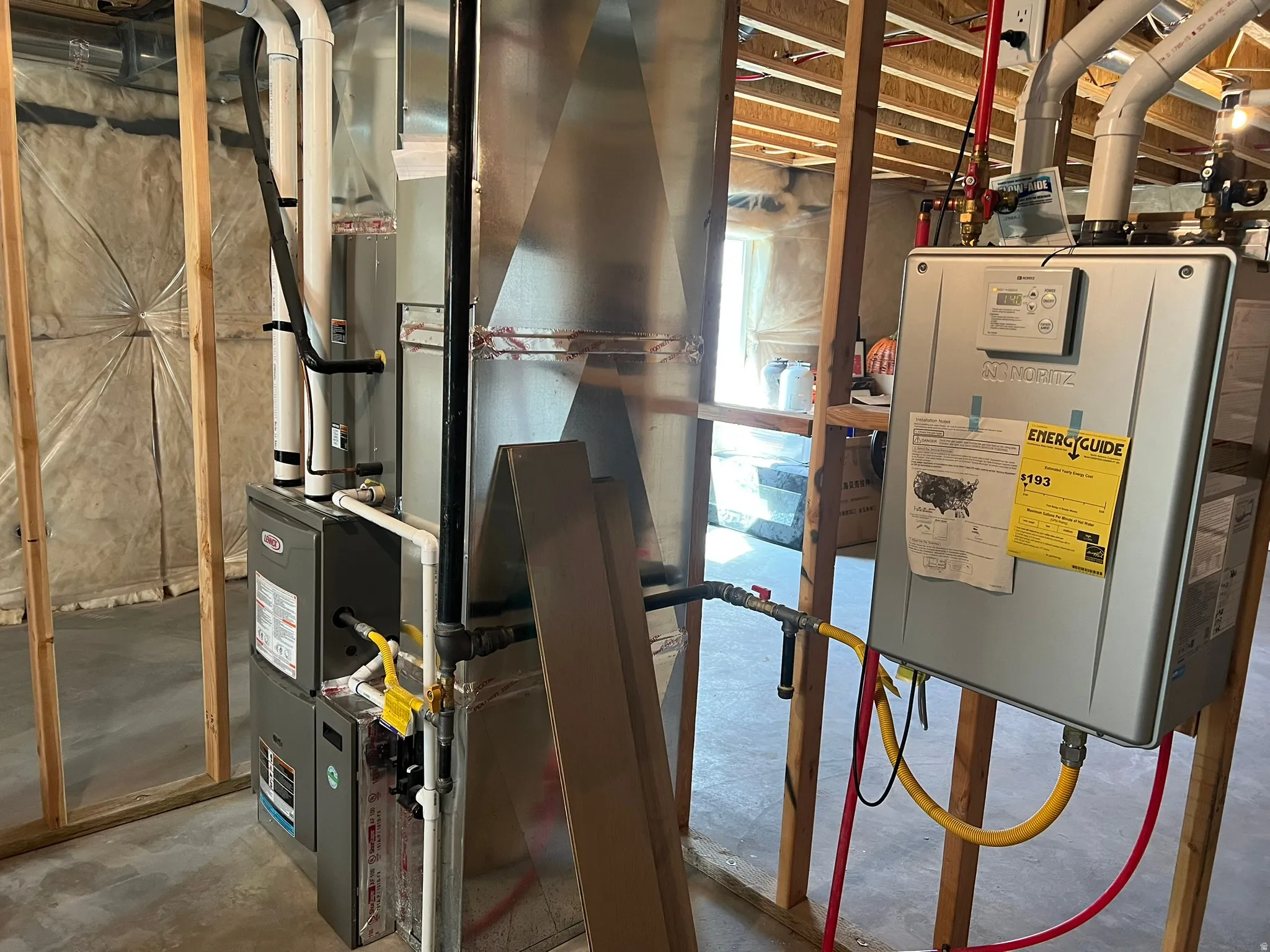 Unfinished utility space featuring a tankless water heater, furnace unit, and exposed wood framing