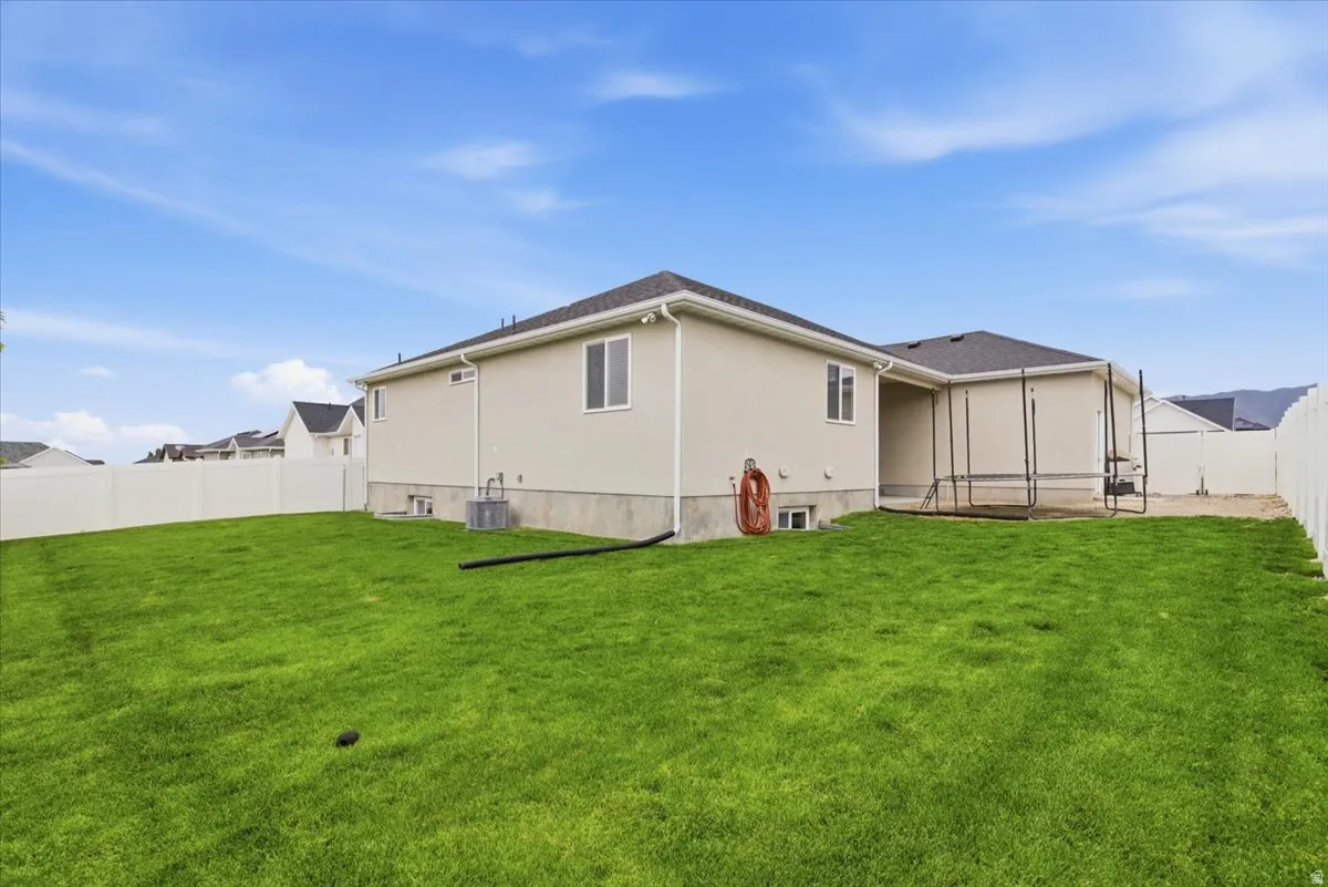 Expansive backyard featuring a manicured lawn, a full vinyl privacy fence, and a covered patio area