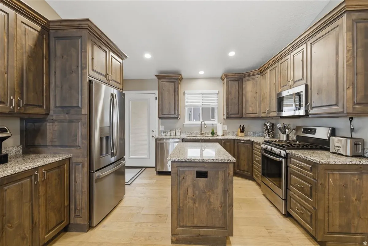 Spacious kitchen featuring extensive wood cabinetry, stone-finish countertops, a central island, and stainless steel appliances