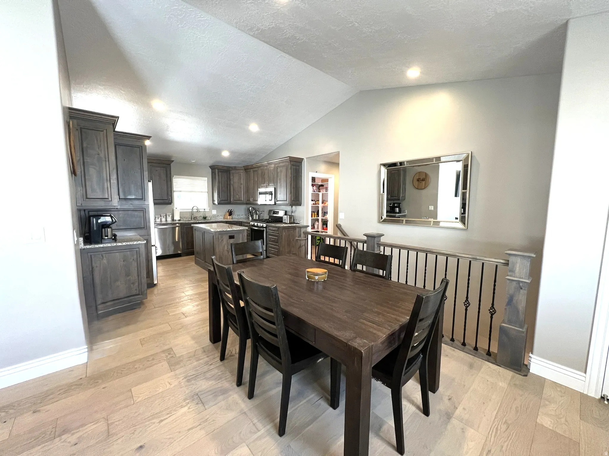 Kitchen and dining area featuring vaulted ceilings, light wood-finish flooring, and recessed lighting