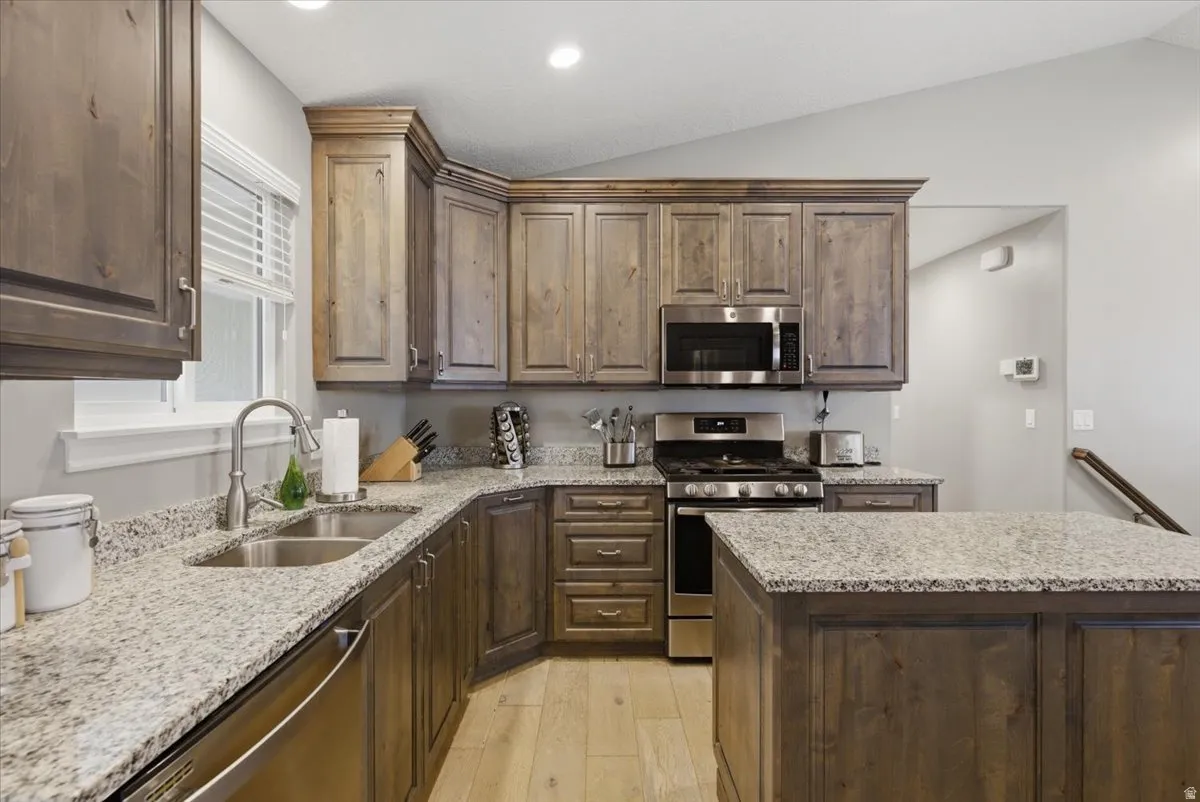 Kitchen featuring wood-finish cabinetry, granite countertops, an undermount double-basin sink, stainless steel appliances, and a central island