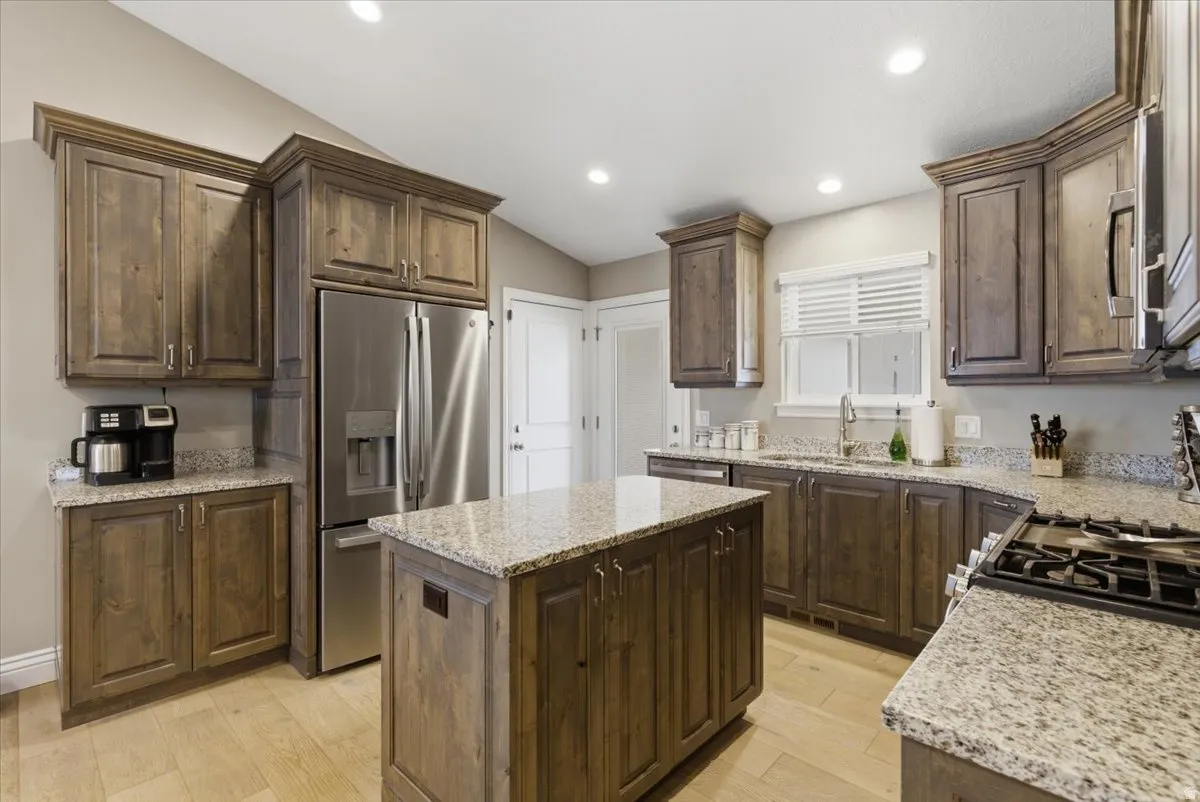 Kitchen featuring wood-finish cabinetry, granite countertops, a central island, stainless steel refrigerator, and a gas range