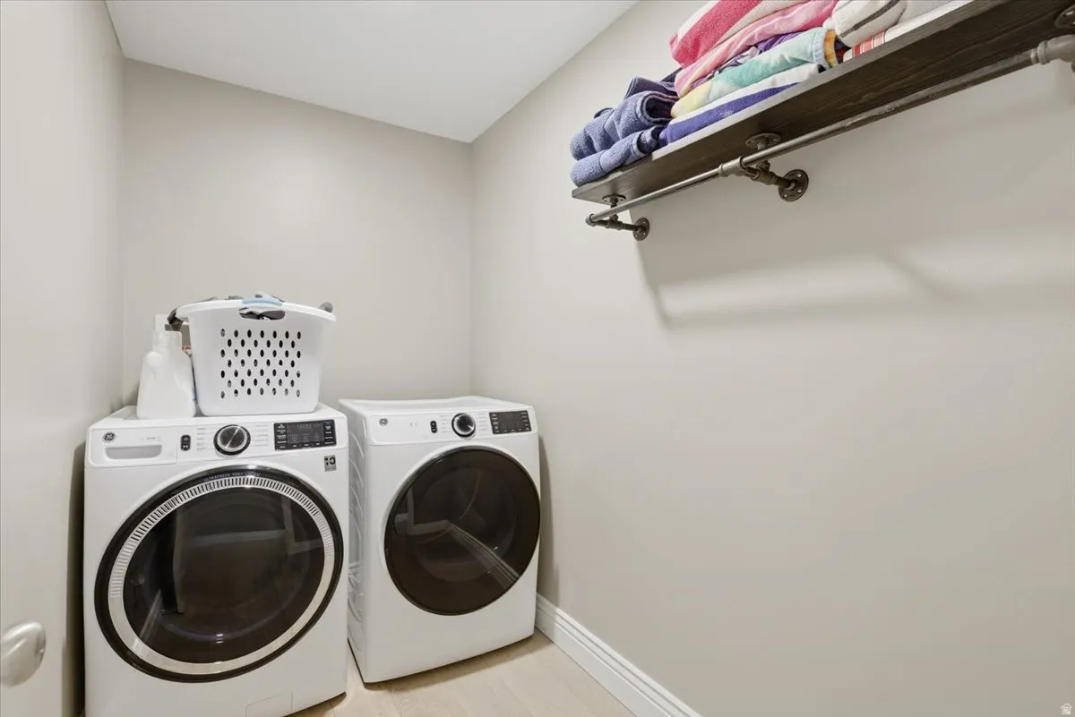 Dedicated laundry space featuring a side-by-side washer and dryer, light-toned wall paint, and a wood-finish shelf with industrial-style pipe supports