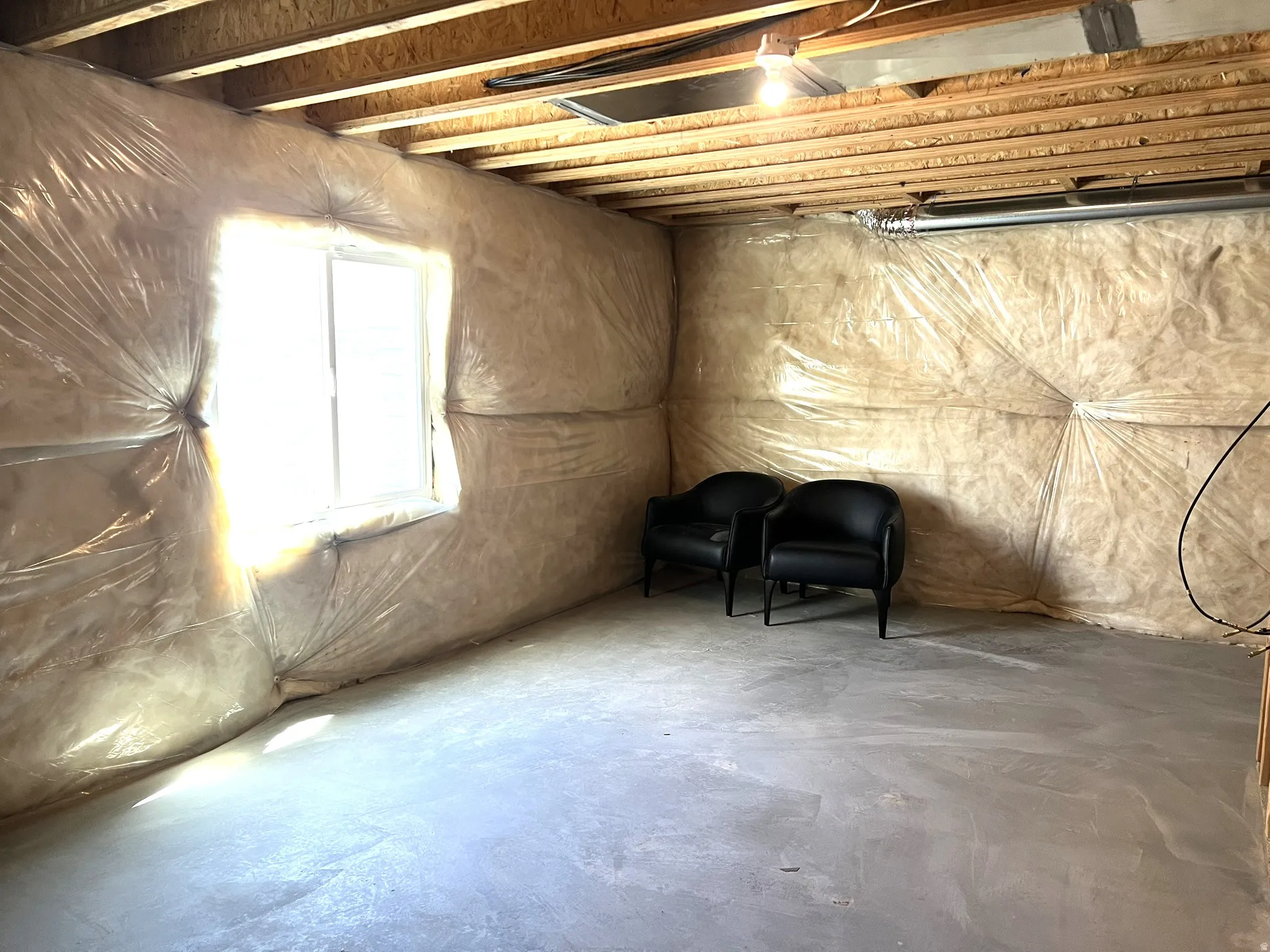 Unfinished basement space featuring a window, exposed ceiling joists, and concrete flooring