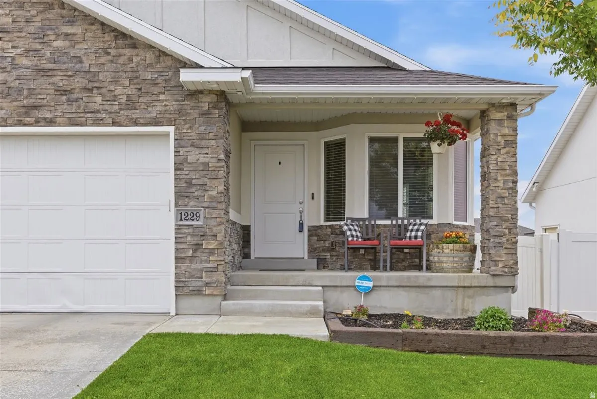 Stone veneer facade featuring a covered porch, white paneled garage door, and a bay window