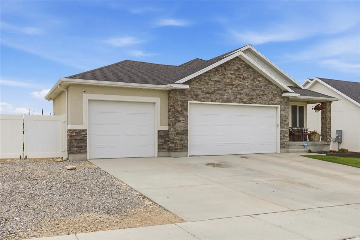 Exterior featuring stone veneer and stucco finishes, a two-car garage with white panel doors, a covered porch entry, and a white vinyl privacy fence