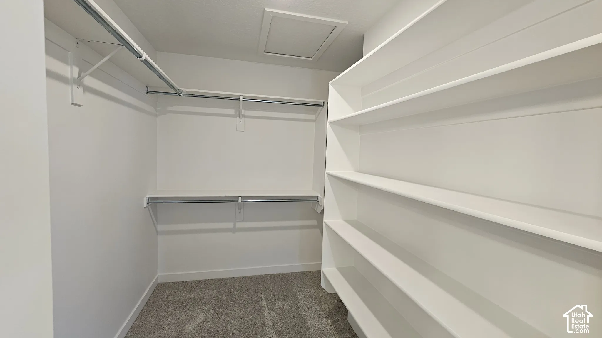 Walk-in closet featuring built-in shelving, dual hanging rods, light gray carpet, white walls, and a ceiling access panel