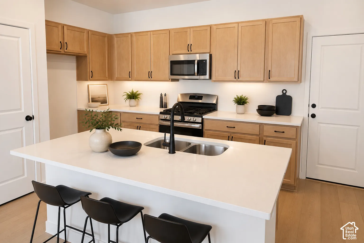 Kitchen featuring light wood cabinetry, stainless steel appliances, a center island with double sink, and light-toned countertops