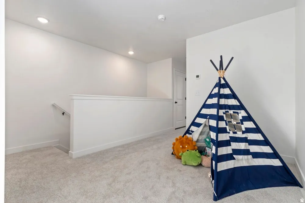 Upper-level landing featuring light gray carpet, white walls, recessed lighting, and a white balustrade