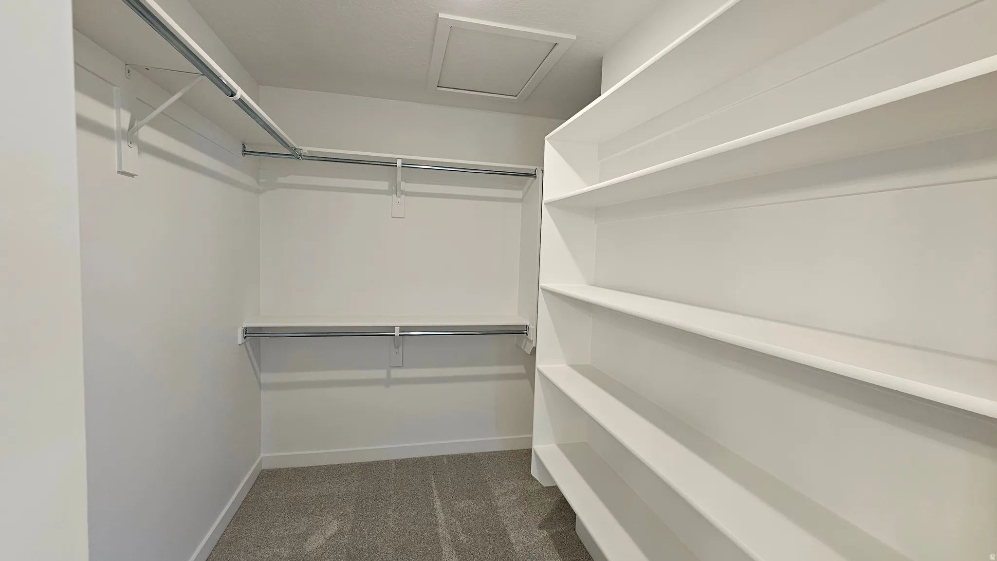 Walk-in closet featuring built-in shelving, dual hanging rods, light gray carpet, white walls, and a ceiling access panel