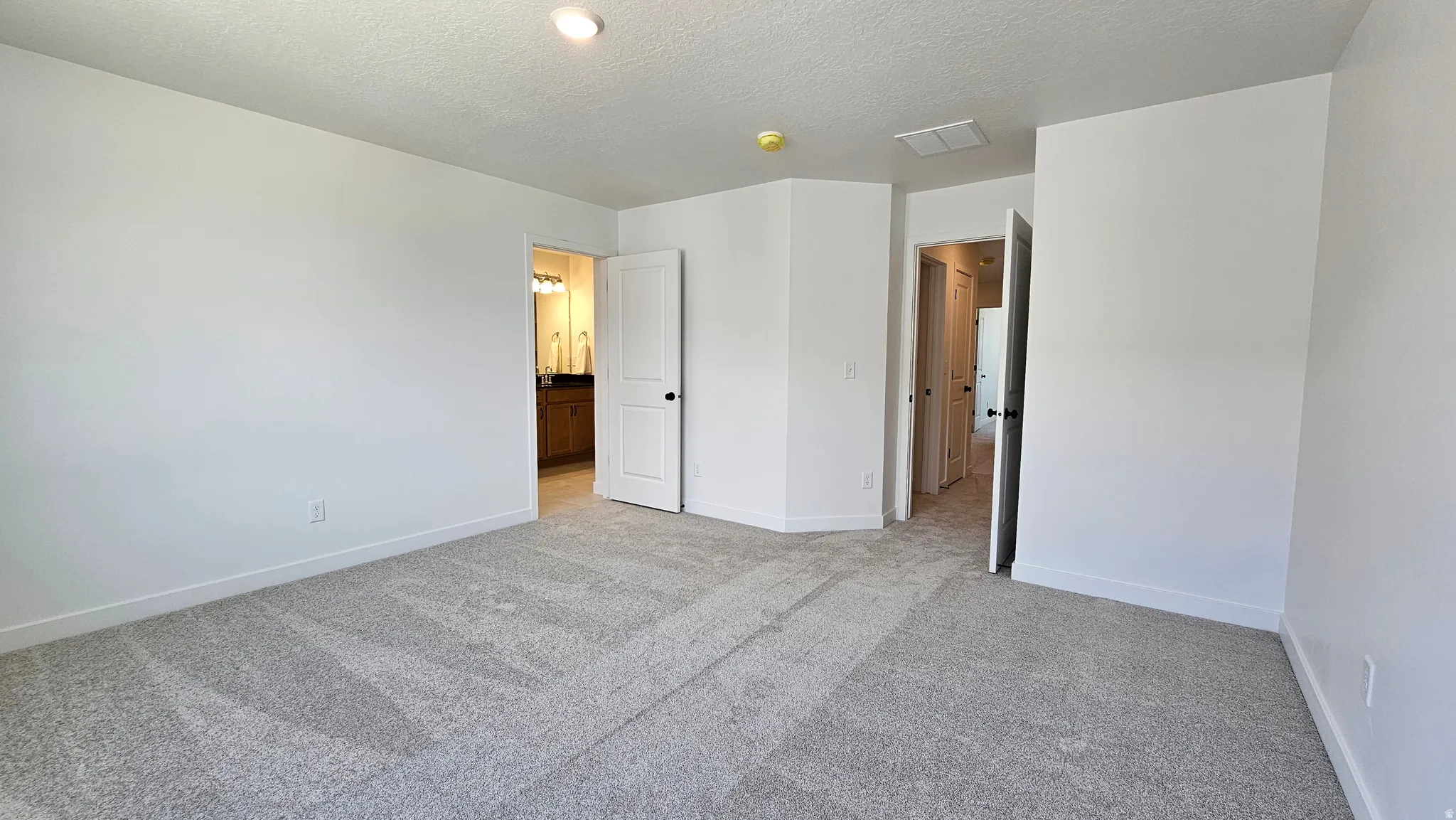 Spacious carpeted room featuring light gray walls and white baseboards