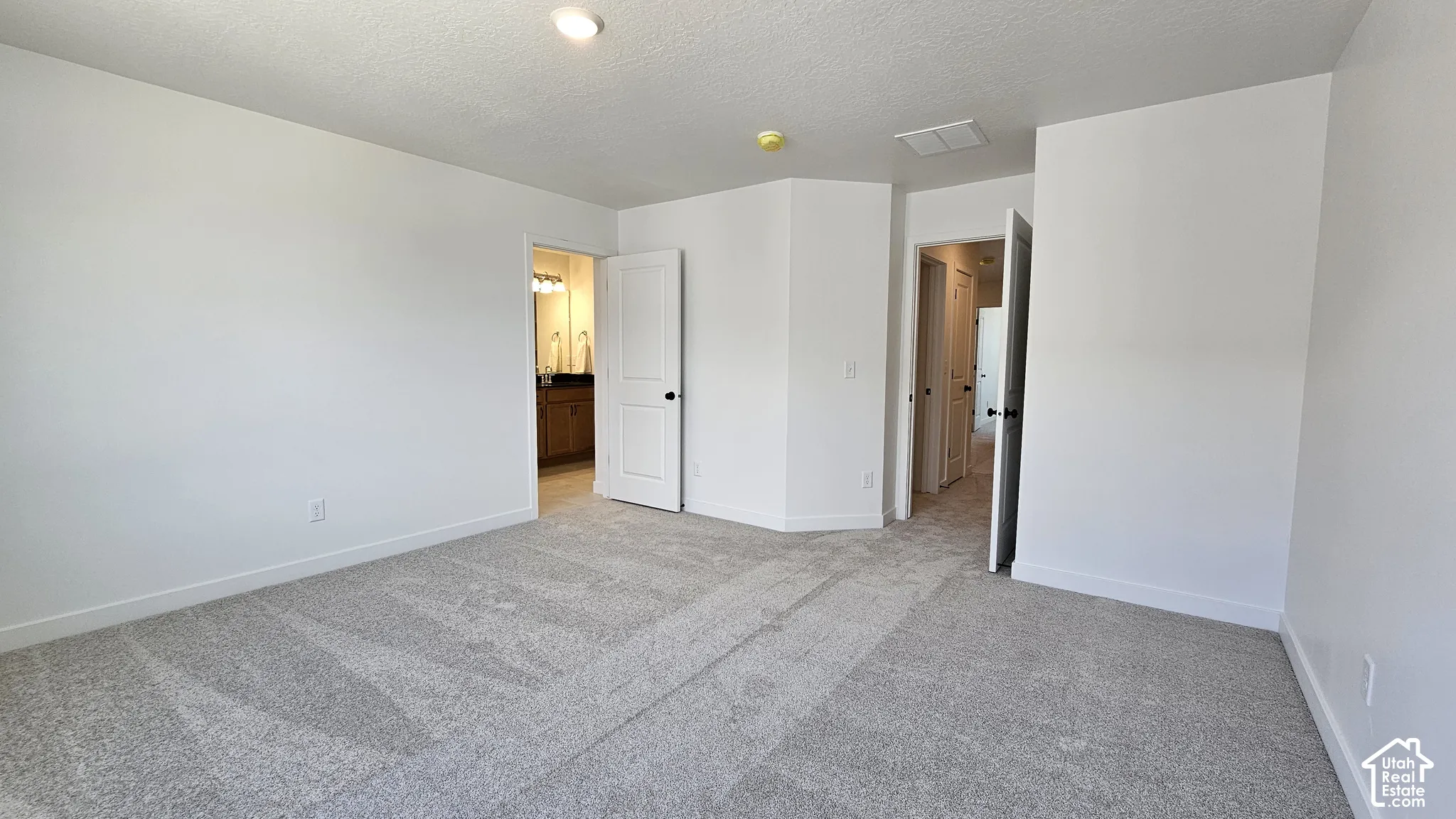 Spacious carpeted room featuring light gray walls and white baseboards