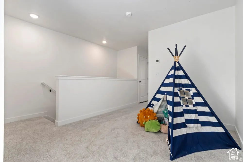 Upper-level landing featuring light gray carpet, white walls, recessed lighting, and a white balustrade