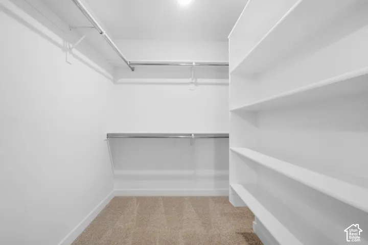 Walk-in storage space featuring multi-level metal clothing rods, custom white built-in shelving, and neutral carpeting