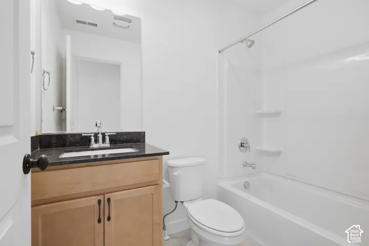 Bathroom featuring a wood-finish vanity cabinet, dark stone countertop, integrated sink with a chrome faucet, and a tub-shower combination with an integrated surround