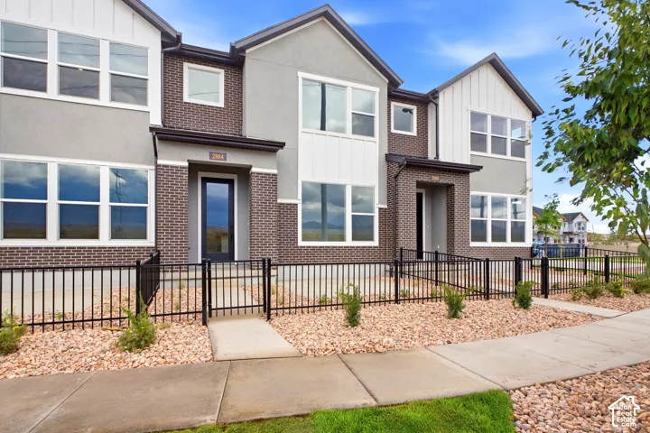 Exterior facade featuring brick masonry, stucco siding, vertical paneling, expansive multi-pane windows, and black metal fencing