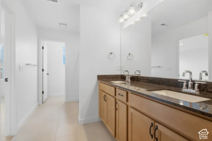 Double vanity featuring a stone countertop, dual undermount sinks, wood-finish cabinetry, and a full-width wall mirror
