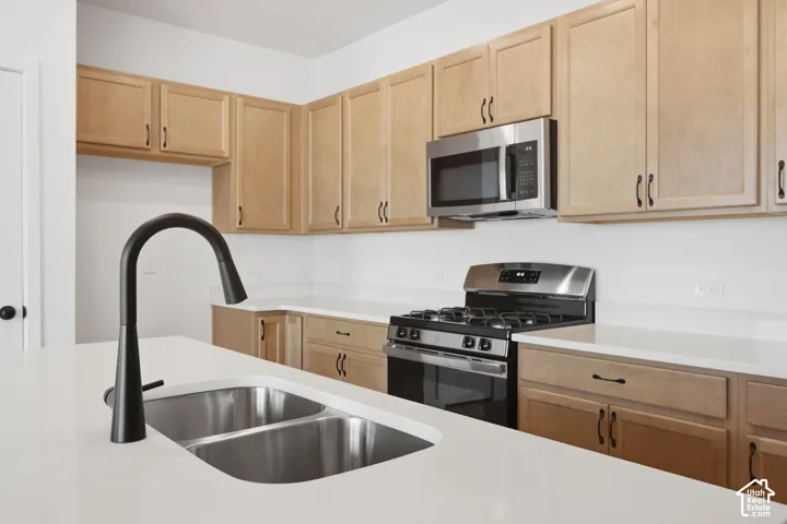 Kitchen featuring light wood cabinetry, white countertops, stainless steel appliances, and a matte black gooseneck faucet with a double-basin undermount sink