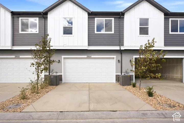 Contemporary townhouse exterior featuring board-and-batten siding, dual-tone facade, attached multi-car garage, and concrete driveway
