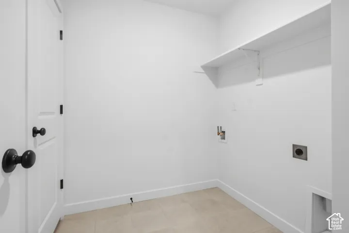 Utility space featuring neutral tile flooring, built-in wall shelving, laundry hookups, and matte black hardware on a solid-core interior door