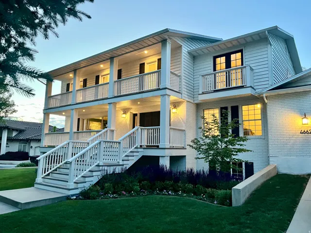 White brick and siding exterior with a multi-level porch, featuring recessed lighting, a prominent staircase, and dark-framed windows
