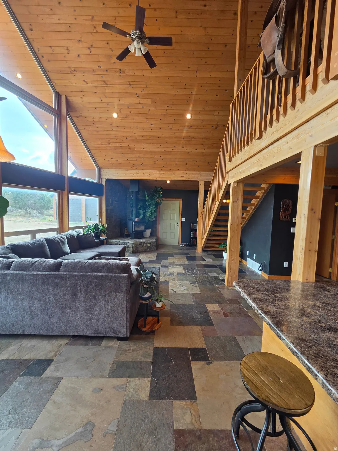 Vaulted tongue & groove ceilings featuring a ceiling fan, expansive wall of windows, multi-tone slate tile flooring, and a wooden staircase with railing