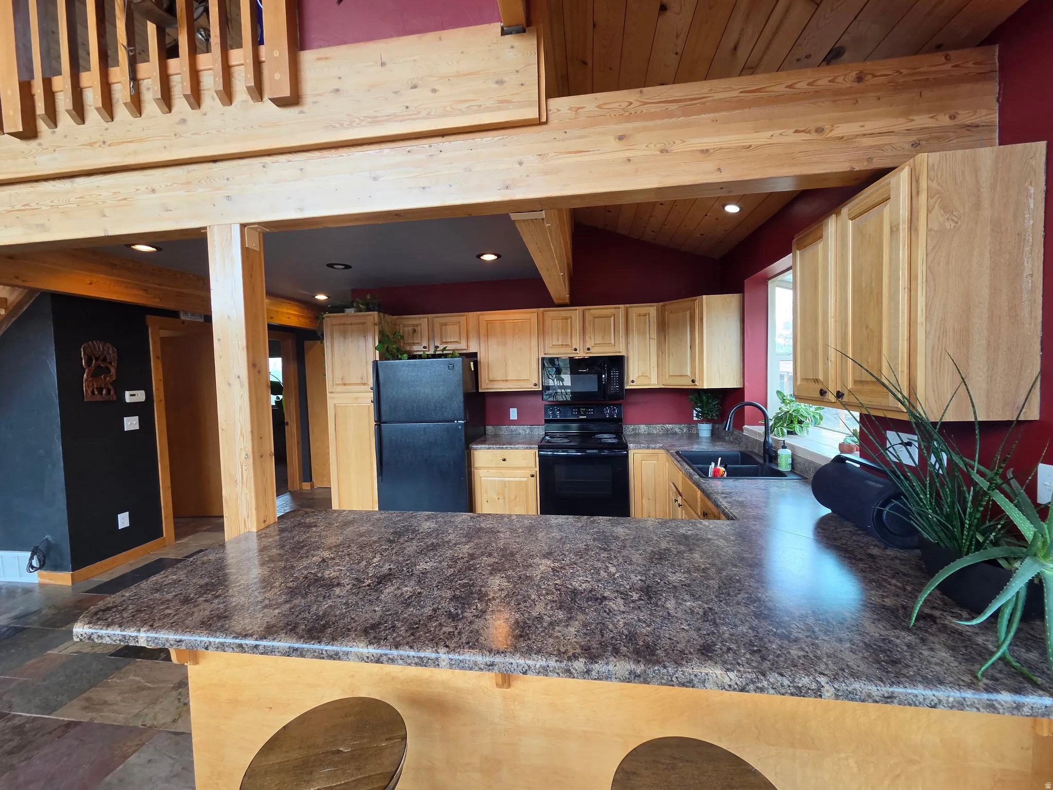 Spacious kitchen featuring light wood cabinetry, black appliances, bar countertop, and an undermount sink with a gooseneck faucet