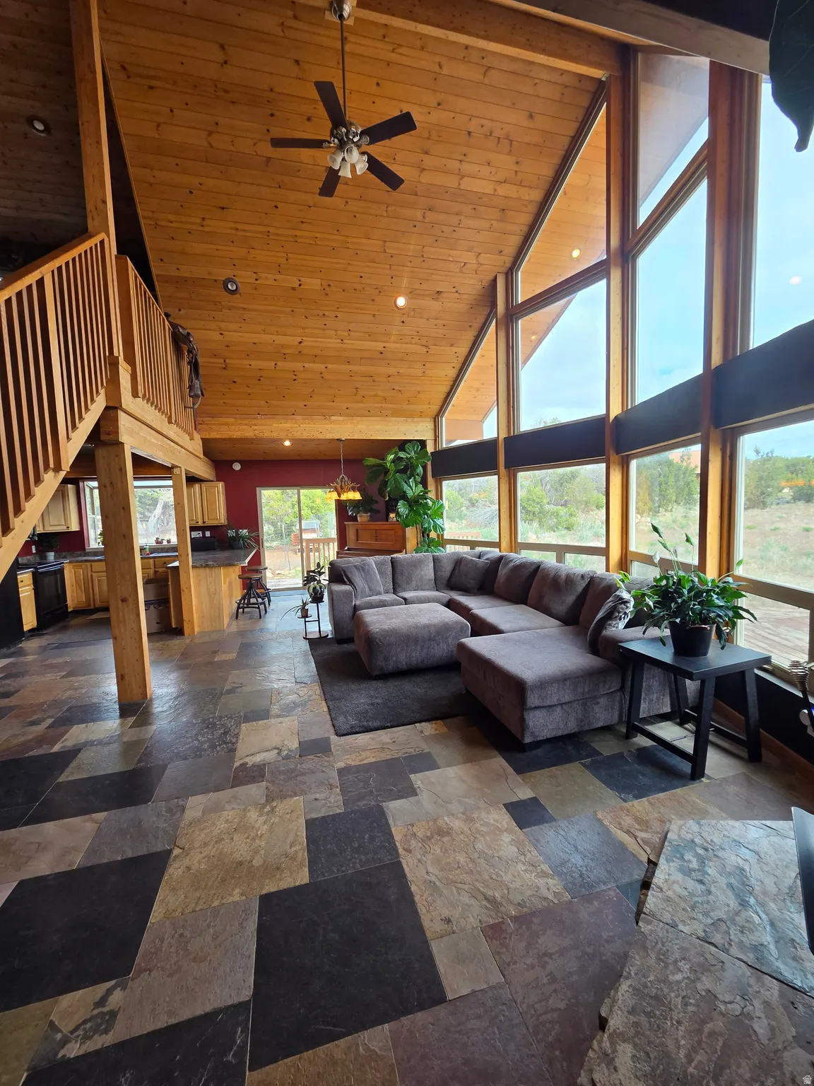 Vaulted tongue & groove ceilings featuring a ceiling fan, expansive wall of windows, multi-tone slate tile flooring, and a wooden staircase with railing